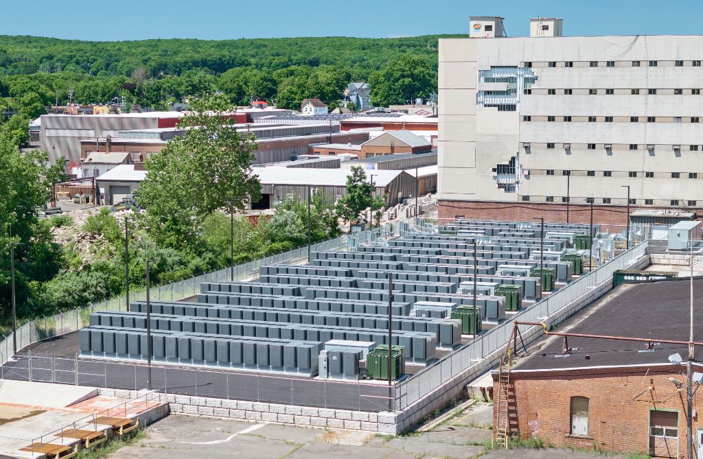 Battery energy storage facility with rows of utility enclosures